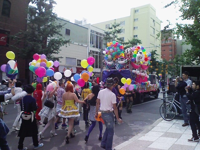 写真：山車と歩く人々、虹色の風船、様々な衣装