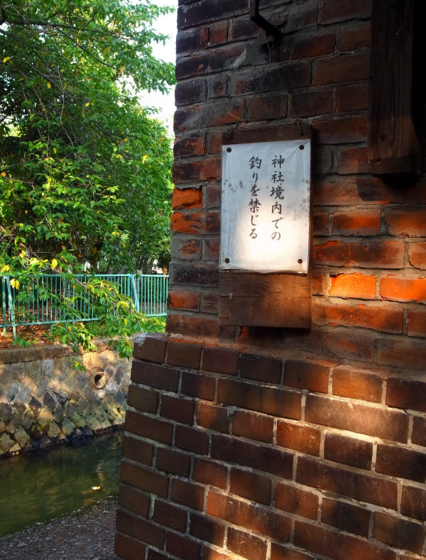 赤レンガの壁面に「神社境内での釣りを禁じる」との貼り紙が鋲でとめられている写真。